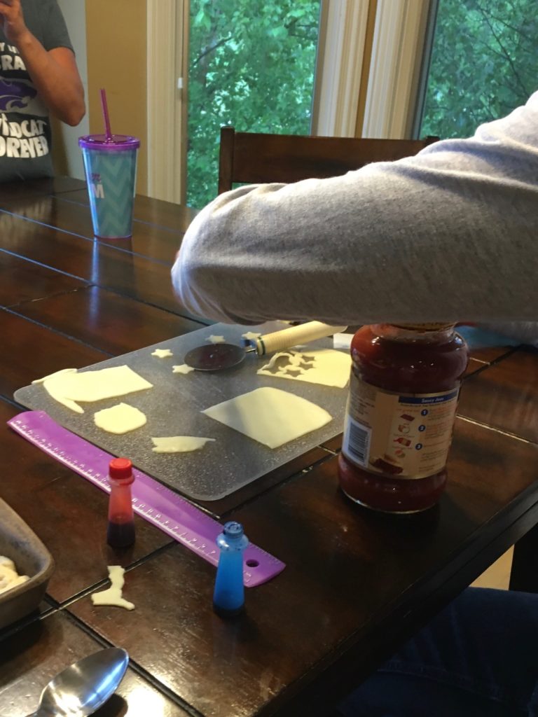 image of mozarella slices being cut with small star shaped cookie cutters.  These cheese cutouts go onto the flag for the pizza