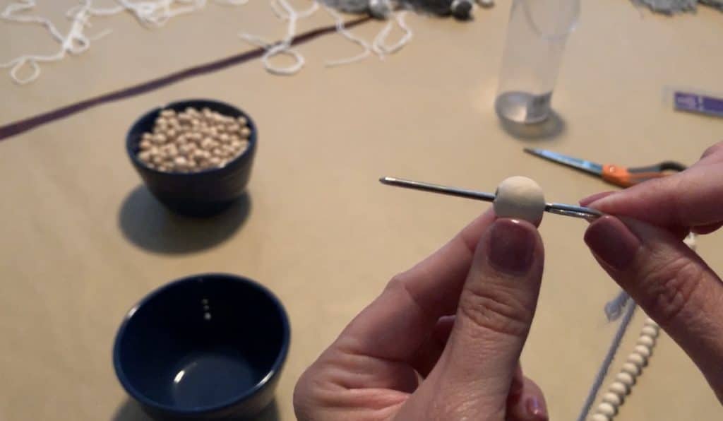 threading a yarn string with a wood bead