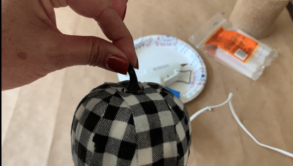 Gluing pumpkin stem back onto fabric covered foam pumpkin for this Halloween decoration DIY project