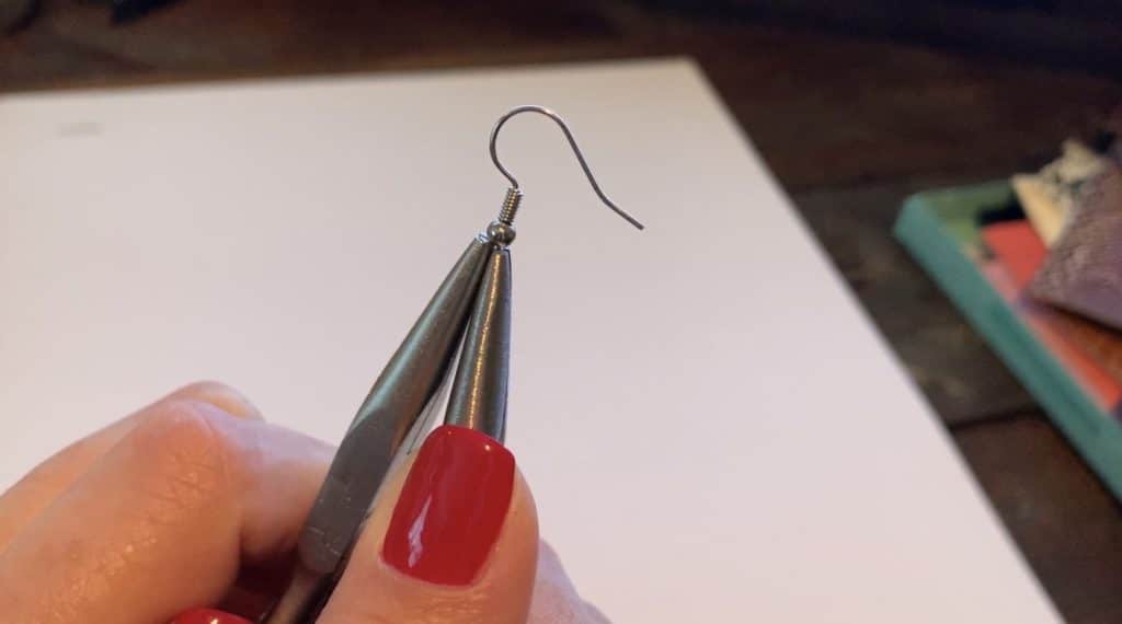 working with the earring hook to open it so that the leather earring can be placed onto the hook