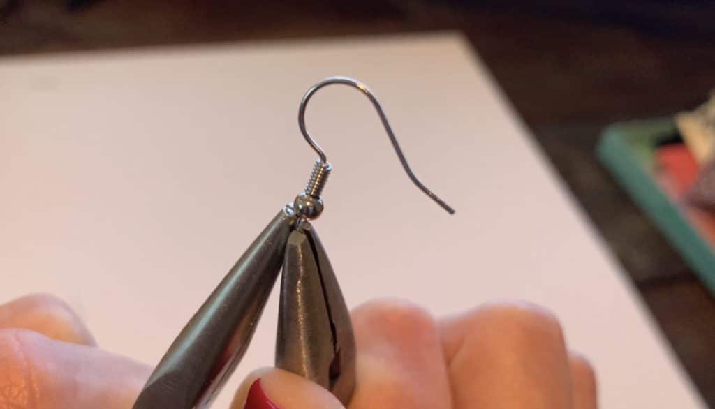 working with the earring hook to open it so that the leather earring can be placed onto the hook