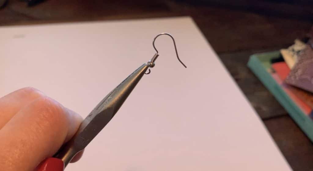 working with the earring hook to open it so that the leather earring can be placed onto the hook