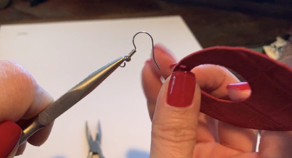working with the earring hook to open it so that the leather earring can be placed onto the hook
