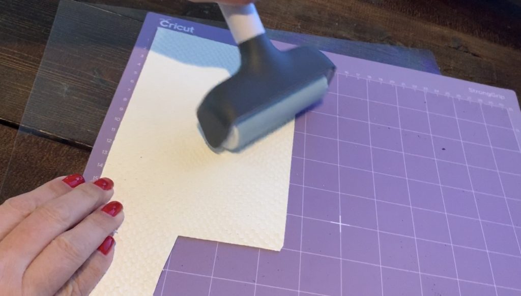 using a Cricut brayer to press leather onto the Cricut mat before cutting the leather earrings diy project