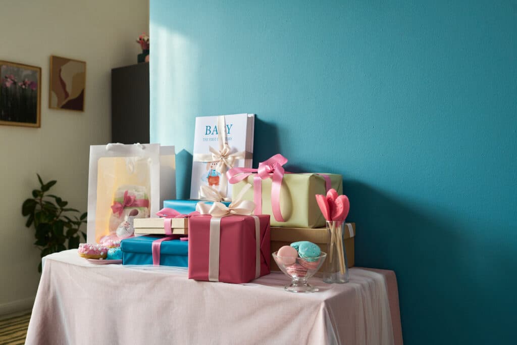 Baby shower gift table with wrapped presents, a parenting book, macarons, lollipops, and a gift bag, illustrating how to plan a baby shower by setting up a dedicated spot for gifts and cards.