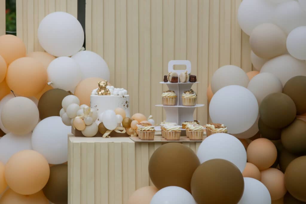 Neutral‑toned baby shower dessert table with balloons, cupcakes, and a bear‑themed cake, illustrating how to plan a baby shower by choosing a cohesive theme.