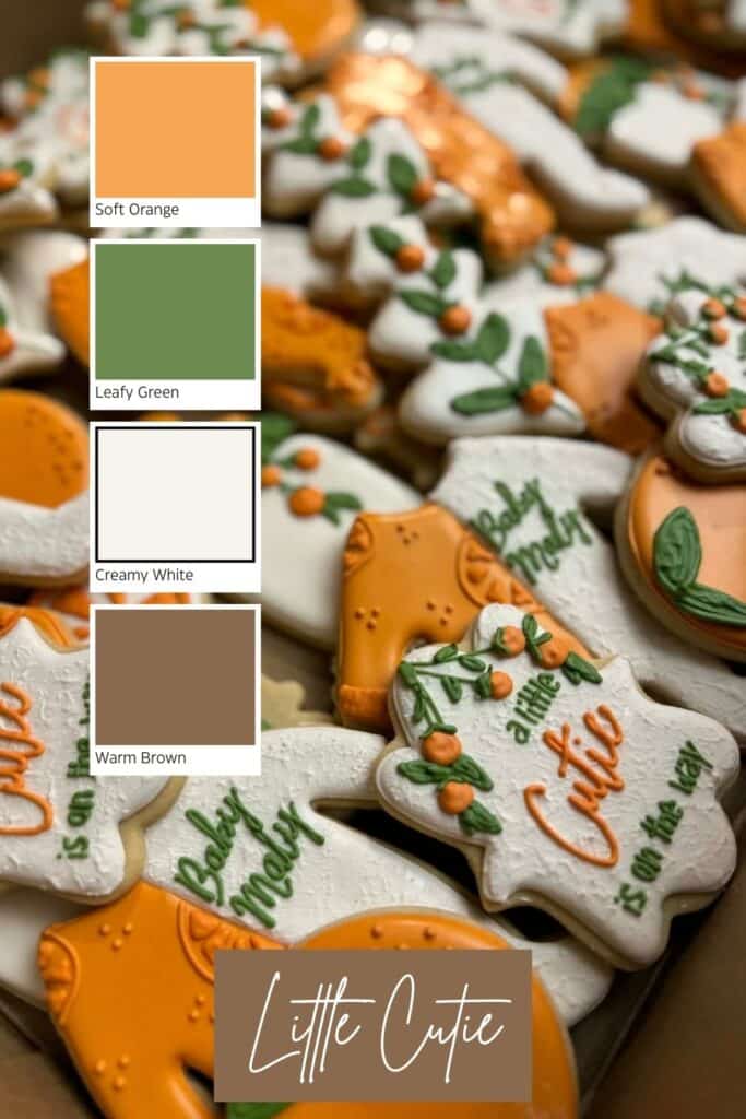 A Little Cutie–themed baby shower backdrop featuring a pastel balloon arrangement with soft oranges, creams, and greenery, styled with citrus accents and a coordinating color palette beside the display.