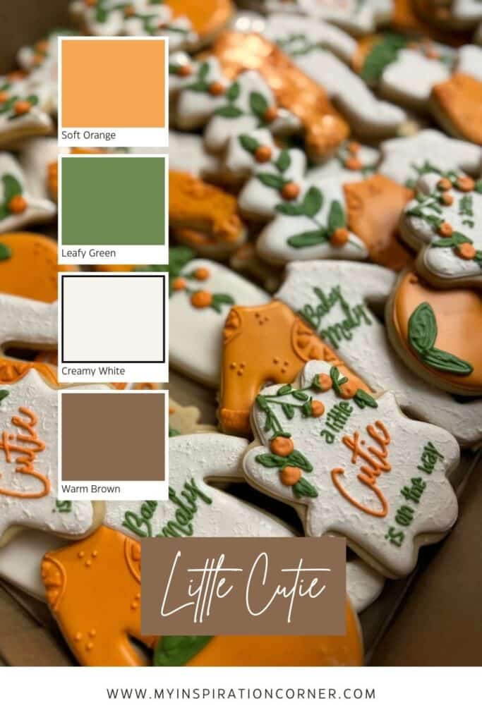 Decorated Little Cutie baby shower cookies arranged in a box, featuring oranges, onesies, and sweet baby‑themed designs in soft orange, leafy green, creamy white, and warm brown icing. A bright and cheerful color palette perfect for a citrus‑themed baby shower.