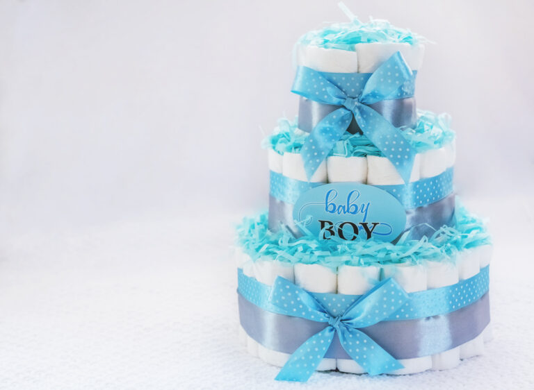 Three‑tier diaper cake decorated with blue and silver ribbon, shredded paper, and a “baby boy” sign, styled as a baby shower centerpiece.