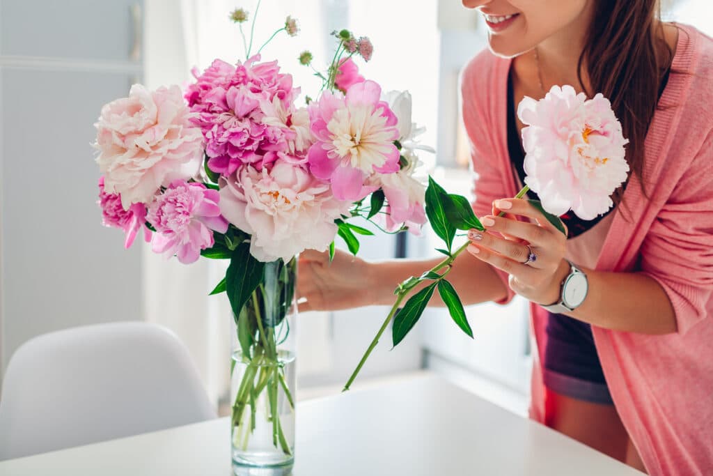 Person arranging a bouquet of pink and white flowers in a clear glass vase, creating a simple and elegant display that could easily be borrowed instead of purchased for a baby shower.