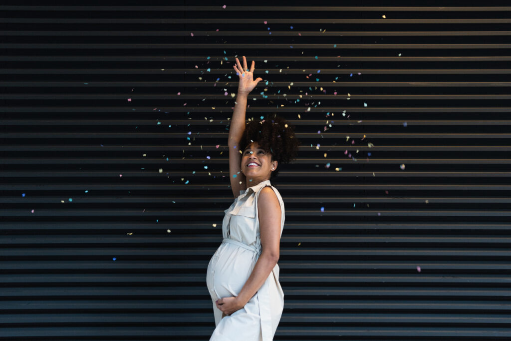 Pregnant woman celebrating with falling confetti, a joyful moment that reflects how to plan a baby shower with simple, meaningful touches.