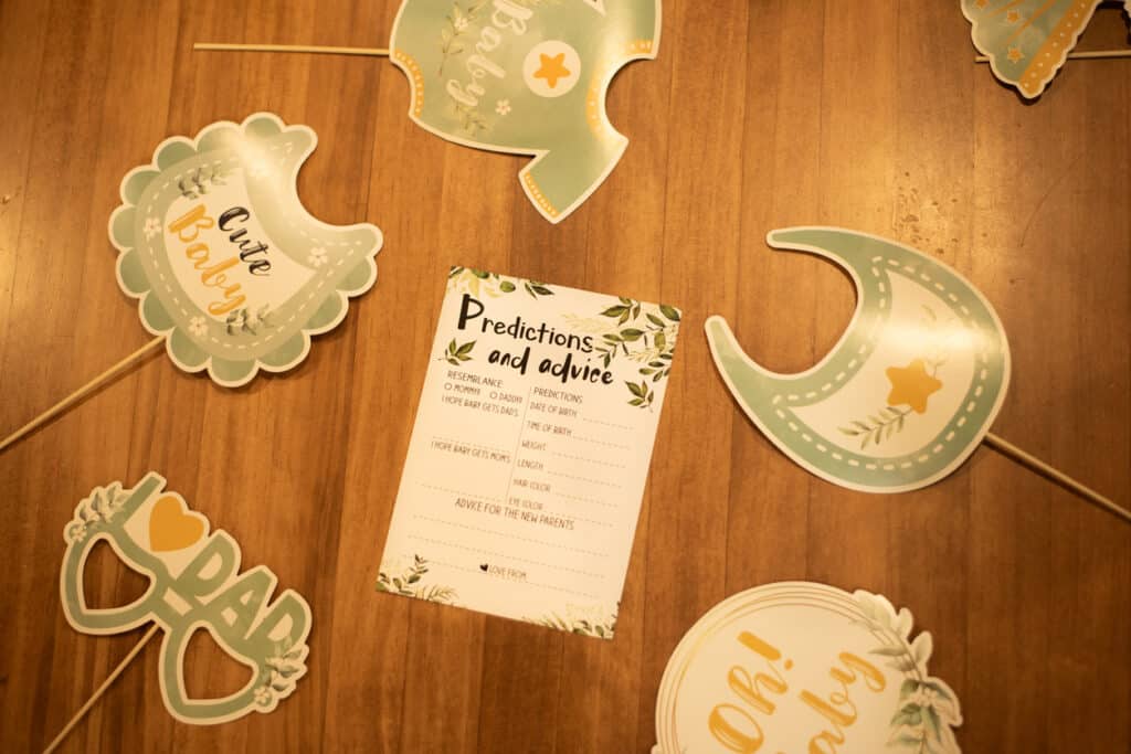 A small tabletop display of neatly arranged baby‑shower photo props, including themed cutouts and a “Predictions and Advice” card, all organized on a wooden surface to keep the setup simple and cohesive.