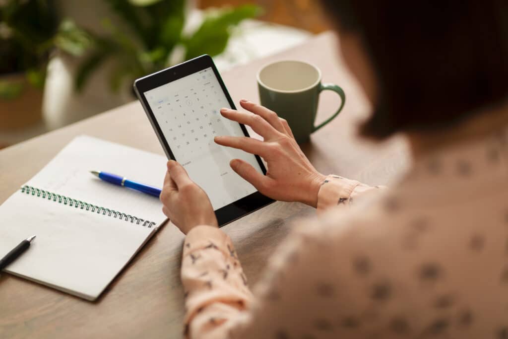 Person using a digital calendar on a tablet to choose a date, illustrating how to plan a baby shower by selecting the best day and location.