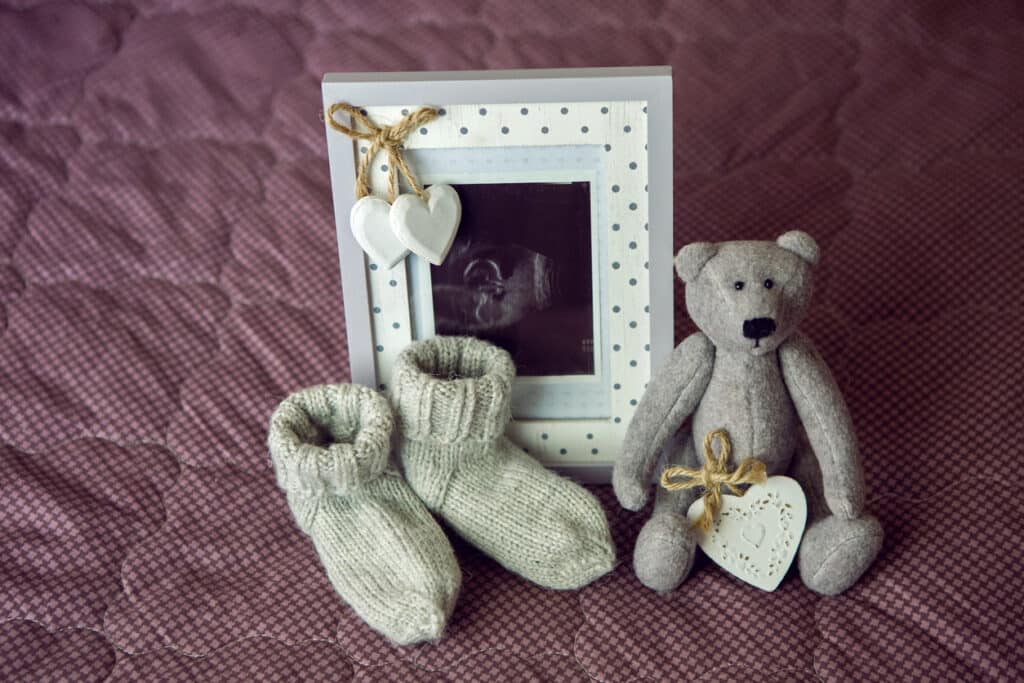 Framed ultrasound photo with baby booties and a soft teddy bear, illustrating how to plan a baby shower by adding meaningful personal touches.