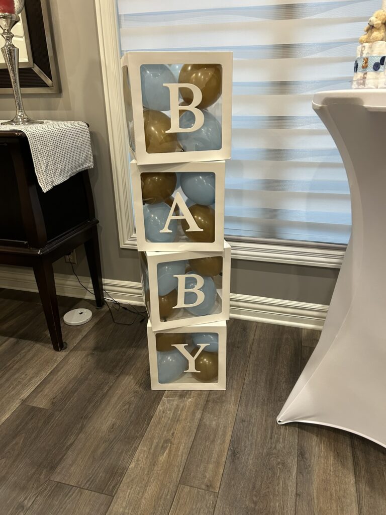 Stacked white baby blocks filled with blue and gold balloons used as themed décor for a We Can Bearly Wait baby shower.