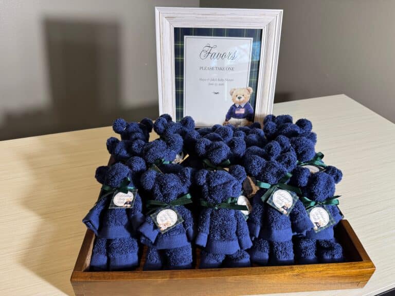 Washcloth bears arranged in a wooden tray with green ribbons and personalized tags, displayed with a framed “Favors” sign at a baby shower.