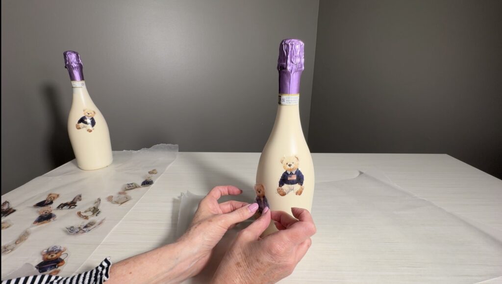 Applying teddy bear image transfers onto a painted bottle during the decorating process.