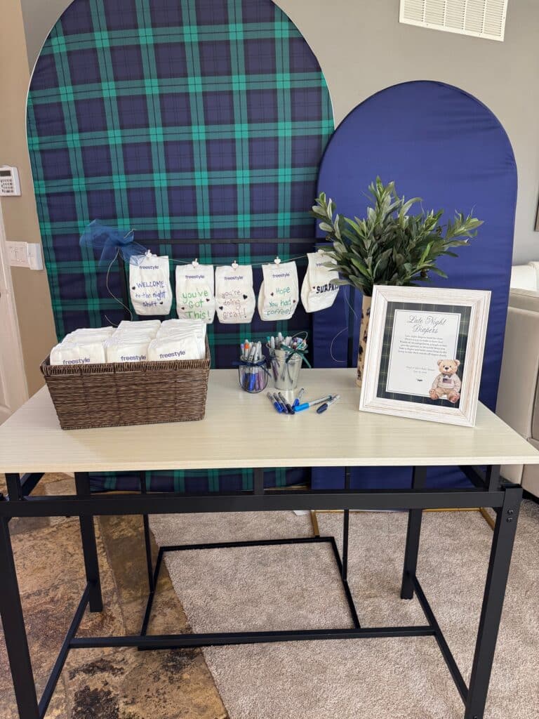 Late‑Night Diaper Notes station at a Classic Polo Bear baby shower, with a plaid backdrop, framed sign, blank diapers, sample decorated diapers, and jars of markers on the table.