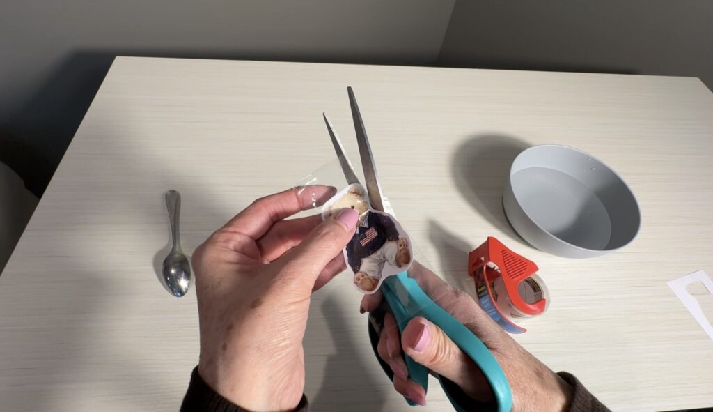 Hands cutting around a taped teddy bear design with scissors after the tape has been applied.