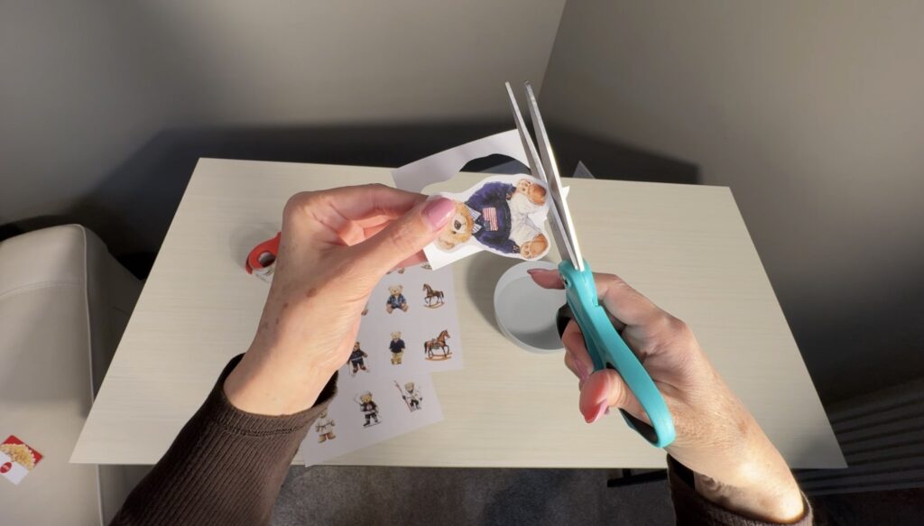 Hands cutting out a printed teddy bear illustration with scissors as part of the tape image transfer process.