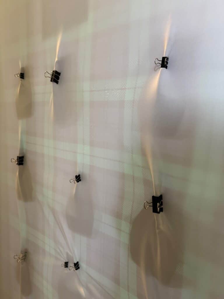 Back of an arch backdrop showing plaid fabric secured with evenly spaced black binder clips along the top edge.