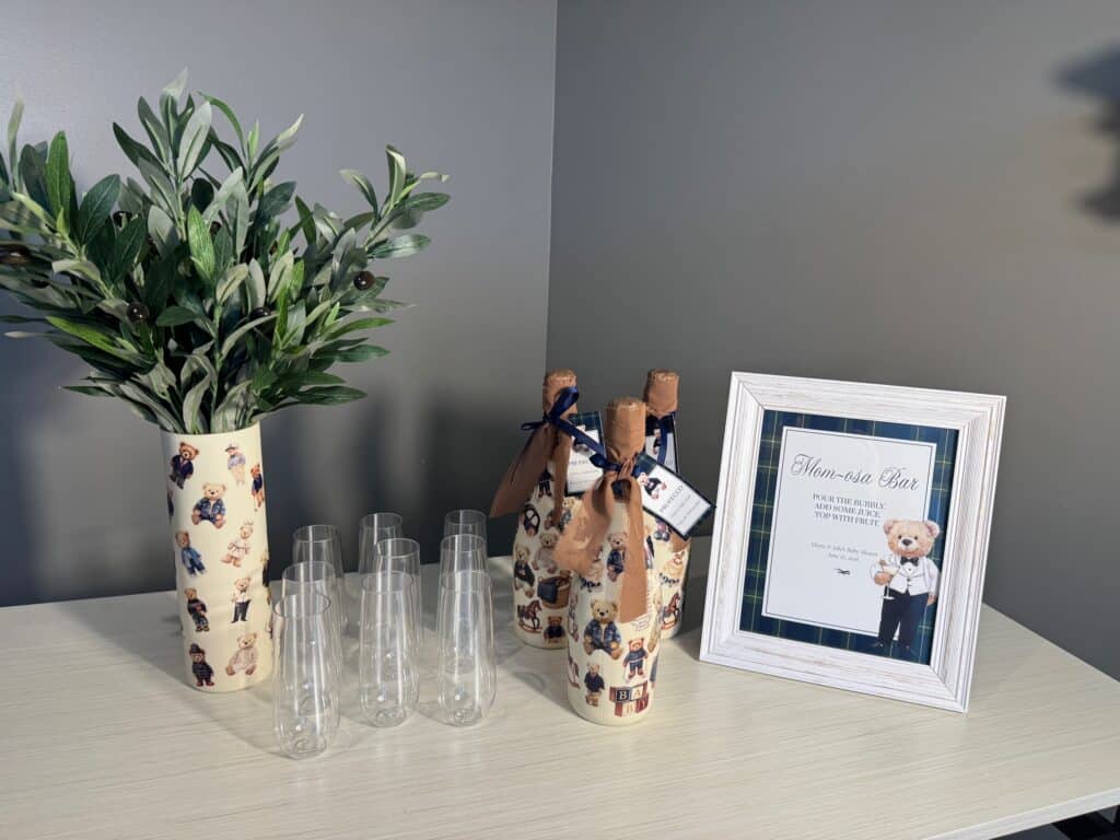 Finished teddy‑bear‑themed bottles arranged with champagne flutes and a framed Mom‑osa Bar sign.