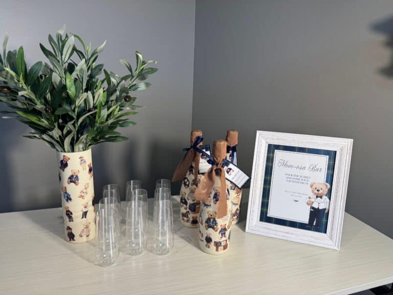 Finished teddy‑bear‑themed bottles arranged with champagne flutes and a framed Mom‑osa Bar sign.