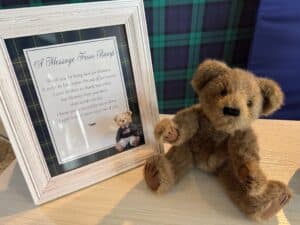Framed “Message From the Bump” baby shower sign displayed beside a plush teddy bear on a wooden surface.