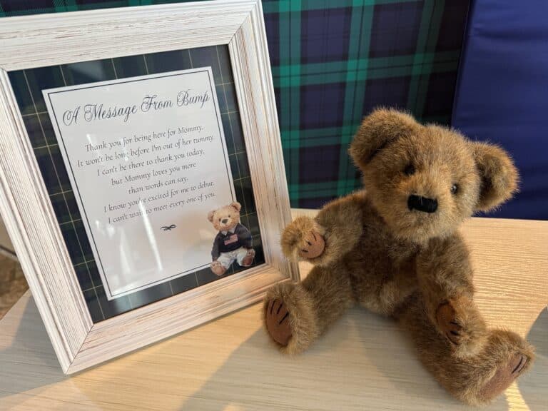 Framed “Message From the Bump” baby shower sign displayed beside a plush teddy bear on a wooden surface.