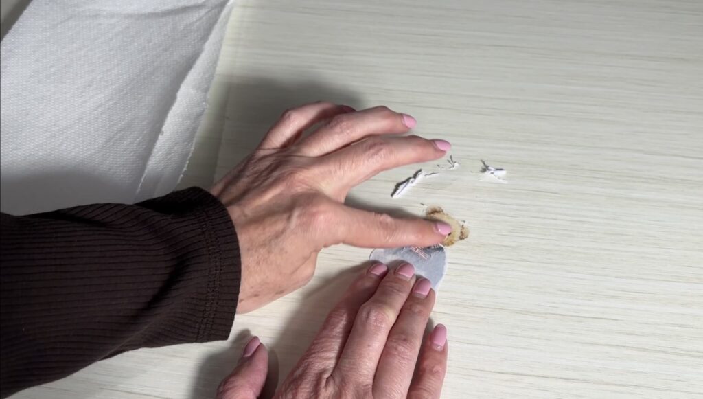 Hands rubbing the paper backing off a taped teddy bear image after soaking it in water.