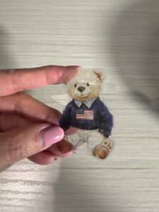 Hand holding a finished clear tape transfer featuring a teddy bear design.